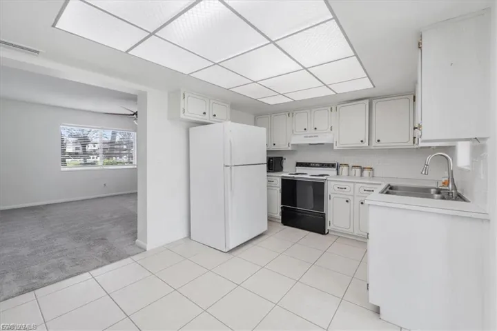 Kitchen with light countertops, white appliances, tasteful backsplash, light tile patterned floors, and light carpet