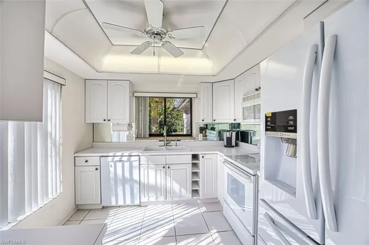 Kitchen with white appliances, a raised ceiling, light countertops, ceiling fan, and white cabinetry