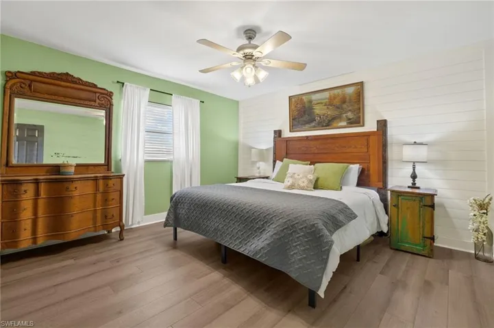 Bedroom with light hardwood / wood-style floors, wooden walls, and ceiling fan