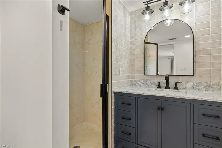 Bathroom with vanity, walk in shower, tile walls, and backsplash