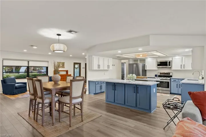 Kitchen featuring white cabinets, pendant lighting, blue cabinetry, appliances with stainless steel finishes, and light hardwood / wood-style floors