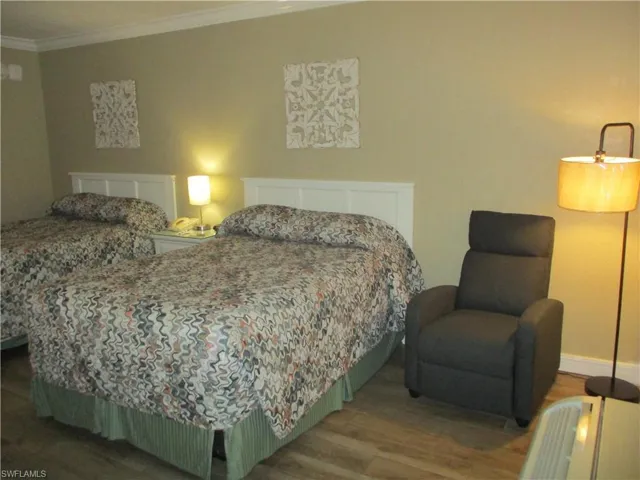 Room with wood tile floors, 2 queen beds, recliner, floor lamp, TV and plenty of storage and ornamental molding