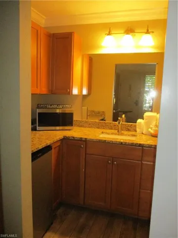 Kitchen with dark wood-type flooring, ornamental molding, brown cabinetry, dishwashing machine, and light stone countertops