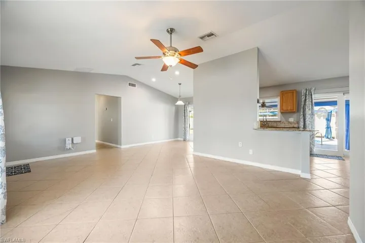 Empty room with ceiling fan, lofted ceiling, and light tile patterned floors