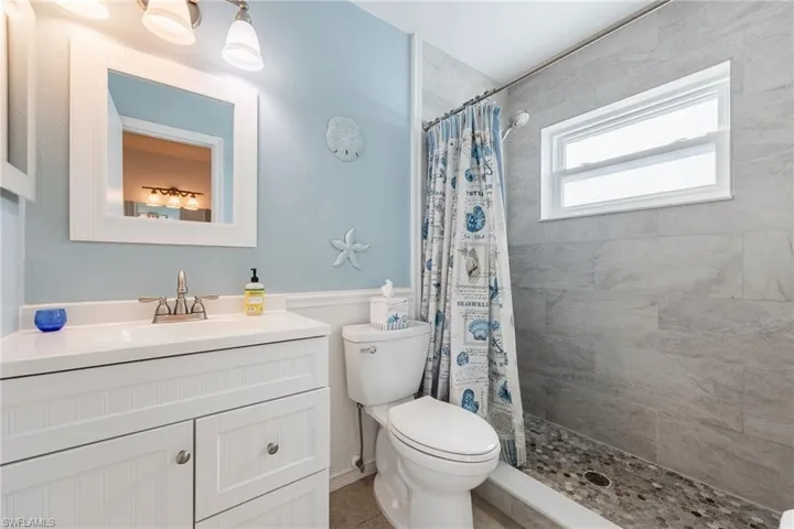 Full bath featuring wainscoting, vanity, tiled shower, and tile patterned flooring
