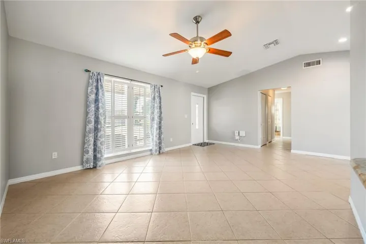 Empty room with a ceiling fan, lofted ceiling, and light tile patterned flooring