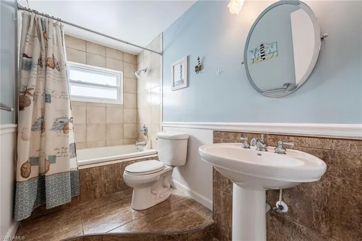 Full bathroom with tiled shower / bath, a wainscoted wall, and tile patterned flooring