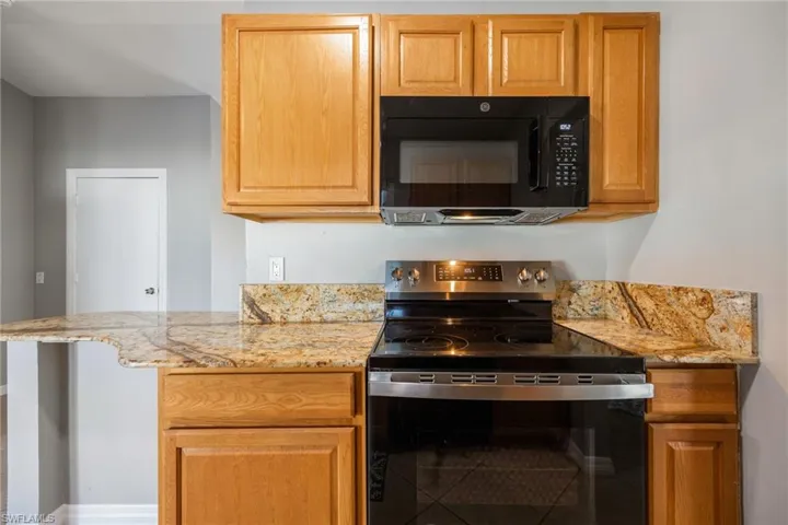 Kitchen featuring stainless steel range with electric stovetop, light stone countertops, black microwave, and brown cabinets