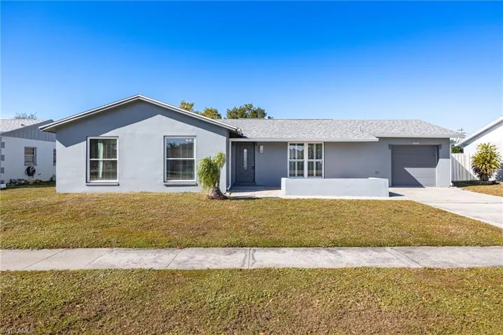 Ranch-style home with stucco siding, a front lawn, and driveway