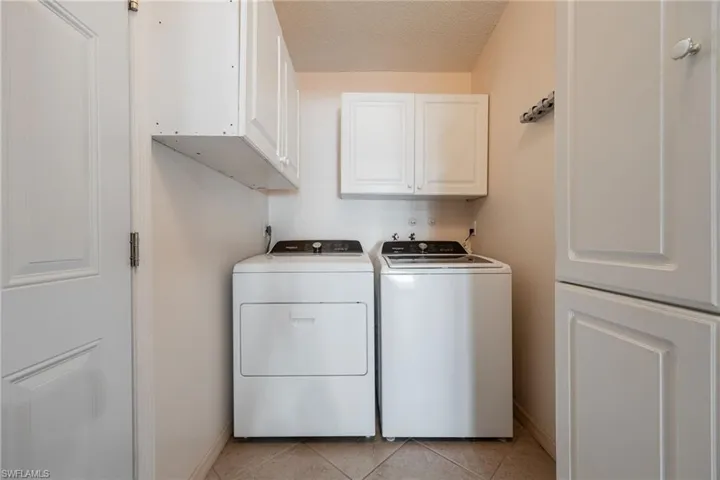 Laundry area with cabinet space, washing machine and clothes dryer, a textured ceiling, and light tile patterned floors