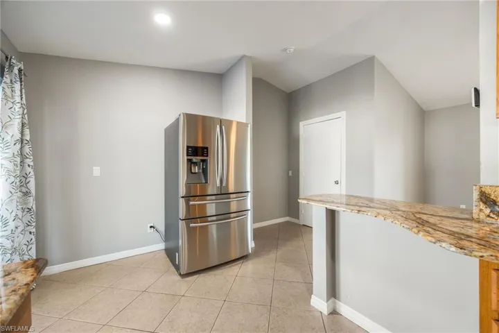 Kitchen featuring stainless steel refrigerator with ice dispenser, light stone counters, light tile patterned flooring, and a peninsula