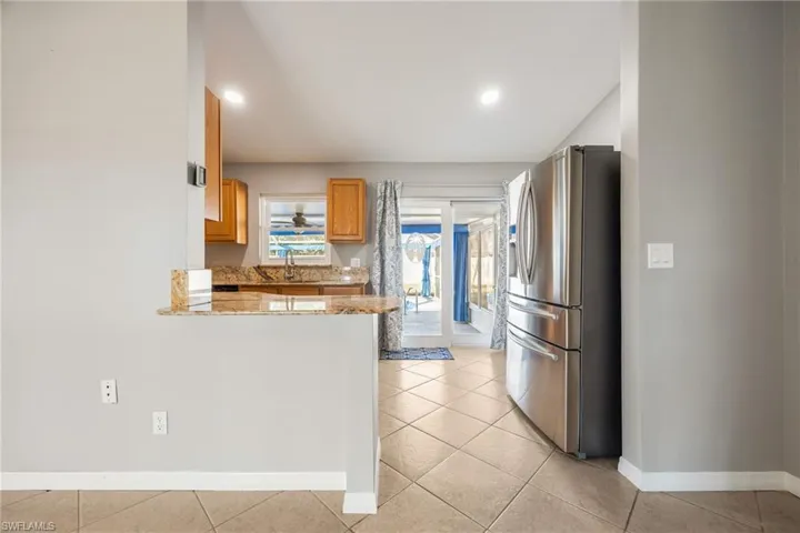 Kitchen featuring stainless steel refrigerator with ice dispenser, light stone countertops, brown cabinetry, light tile patterned flooring, and a peninsula