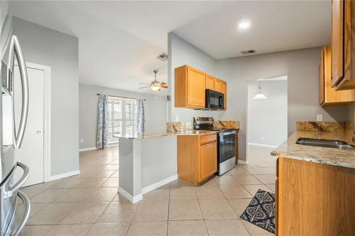 Kitchen featuring light stone counters, stainless steel appliances, light tile patterned floors, and ceiling fan