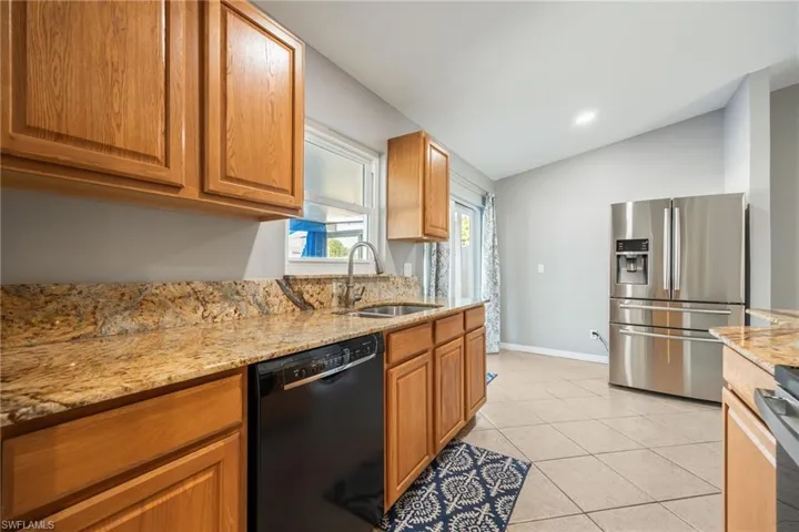 Kitchen with appliances with stainless steel finishes, light stone countertops, brown cabinetry, light tile patterned floors, and vaulted ceiling