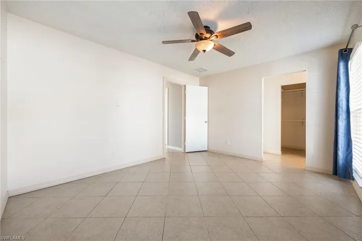 Unfurnished bedroom featuring a spacious closet, a textured ceiling, ceiling fan, and light tile patterned floors