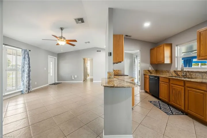 Kitchen with light stone counters, healthy amount of natural light, vaulted ceiling, ceiling fan, and brown cabinets
