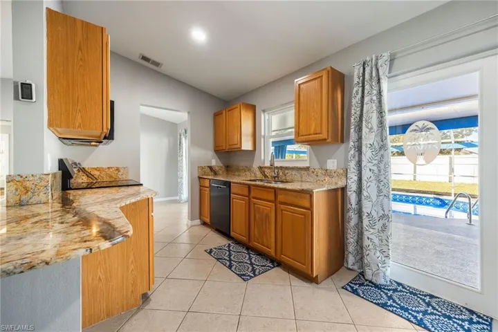 Kitchen featuring light stone counters, vaulted ceiling, light tile patterned flooring, black appliances, and brown cabinets