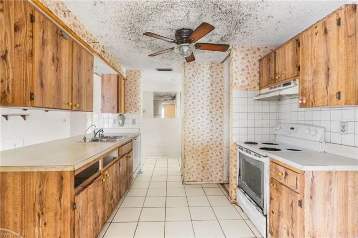 Kitchen featuring white appliances, light countertops, a textured ceiling, wallpapered walls, and ceiling fan