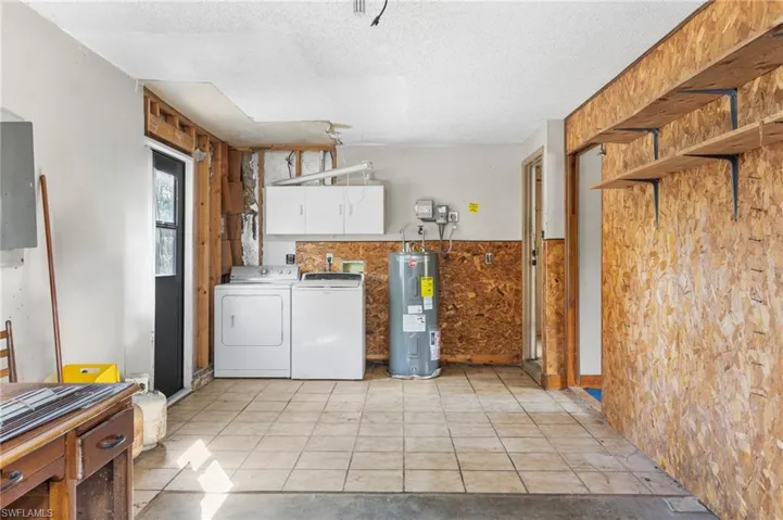 Laundry room with a textured ceiling, washer and clothes dryer, cabinet space, water heater, and wainscoting