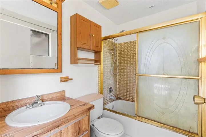 Full bathroom with enclosed tub / shower combo, vanity, and a textured ceiling