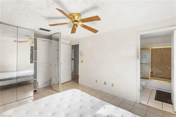 Unfurnished bedroom featuring a textured ceiling, a ceiling fan, ensuite bathroom, and light tile patterned floors