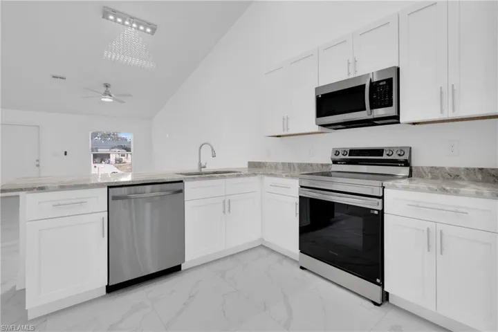 Kitchen featuring stainless steel appliances, a peninsula, light marble finish floors, white cabinets, and high vaulted ceiling