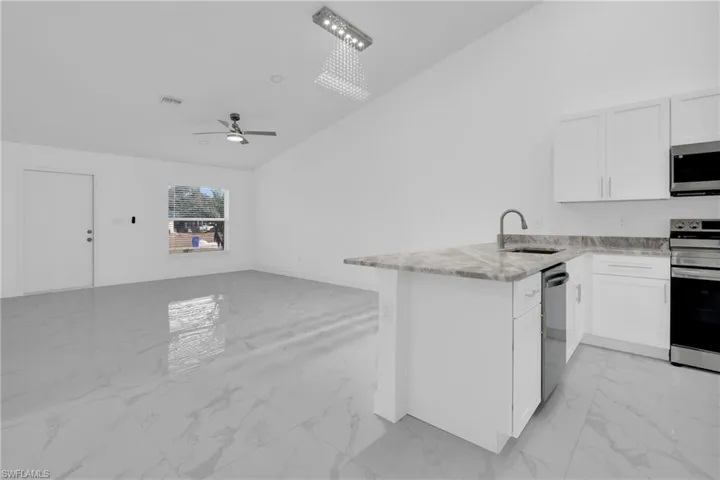 Kitchen featuring light marble finish floors, a peninsula, open floor plan, stainless steel appliances, and lofted ceiling