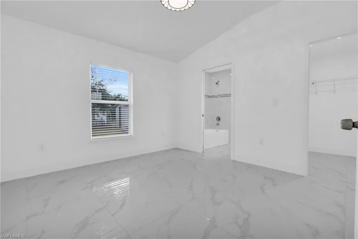 Unfurnished bedroom with light marble finish flooring, vaulted ceiling, and a spacious closet