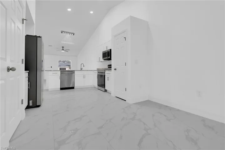 Kitchen with light marble finish floors, white cabinets, stainless steel appliances, high vaulted ceiling, and open floor plan