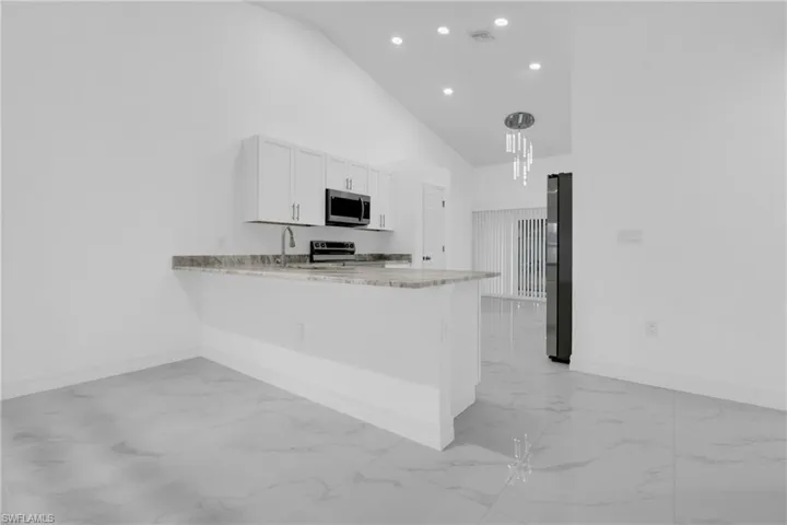 Kitchen featuring high vaulted ceiling, light marble finish floors, light stone counters, a peninsula, and white cabinetry