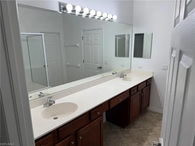Bathroom with double vanity, dark tile patterned flooring, and a shower stall
