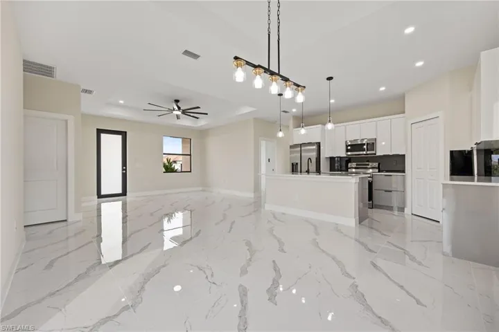 Kitchen with open floor plan, a center island with sink, white cabinets, stainless steel appliances, and decorative light fixtures