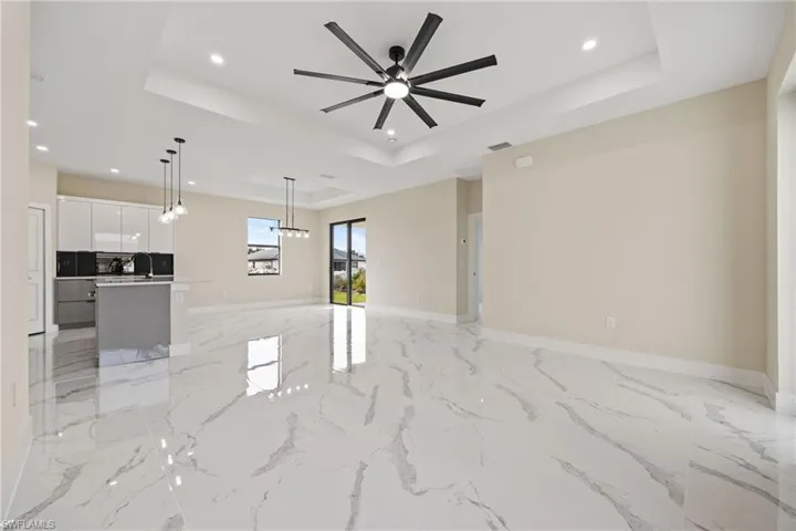 Unfurnished living room featuring recessed lighting, ceiling fan, light marble finish flooring, and a tray ceiling