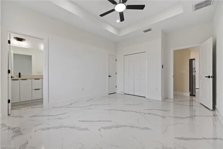 Unfurnished bedroom featuring a tray ceiling, ceiling fan, a closet, and ensuite bath