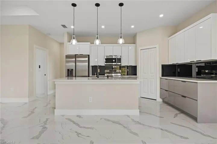 Kitchen with stainless steel appliances, backsplash, decorative light fixtures, and white cabinets