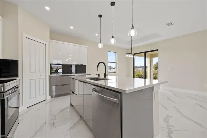 Kitchen featuring stainless steel appliances, modern cabinets, a center island with sink, white cabinets, and light marble finish flooring