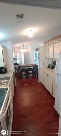 Kitchen with light countertops, white appliances, dark wood-type flooring, a textured ceiling, and decorative light fixtures