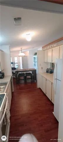 Kitchen with light countertops, white appliances, dark wood-type flooring, a textured ceiling, and decorative light fixtures