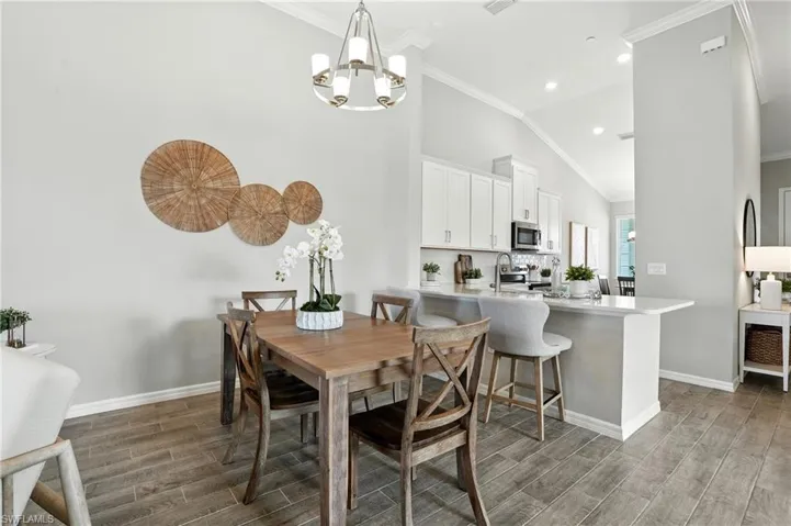 Dining area with light wood finished floors, crown molding, recessed lighting, lofted ceiling, and a chandelier