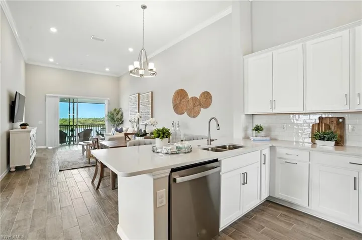 Kitchen with white cabinetry, stainless steel dishwasher, wood tiled floors, open floor plan, and ornamental molding