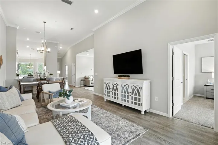 Living room featuring a chandelier, light wood-style flooring, crown molding, recessed lighting, and a high ceiling