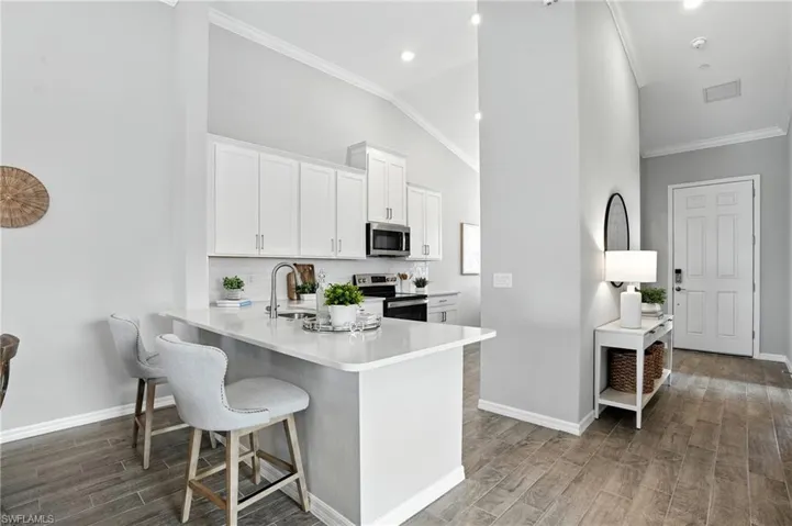 Kitchen with white cabinetry, tasteful backsplash, wood finish floors, a peninsula, and appliances with stainless steel finishes