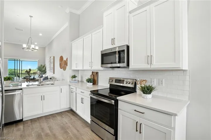 Kitchen featuring stainless steel appliances, white cabinets, decorative backsplash, decorative light fixtures, and light wood-type flooring