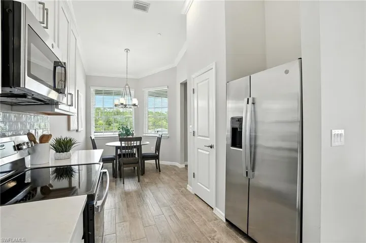 Kitchen featuring appliances with stainless steel finishes, crown molding, light wood-type flooring, a chandelier, and pendant lighting