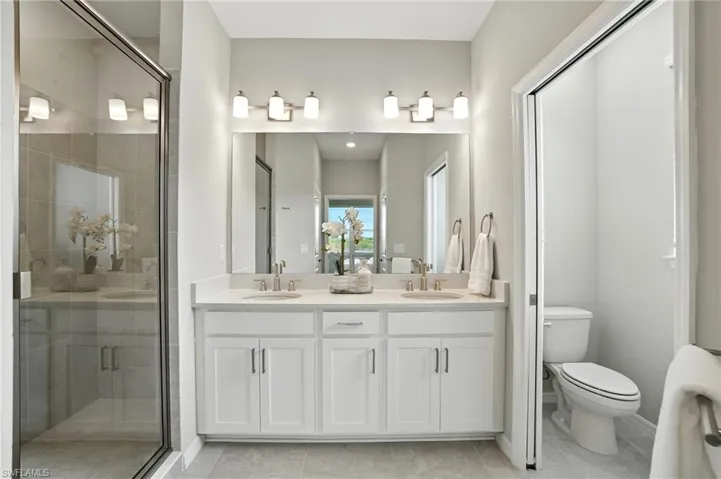 Full bath with a shower stall, double vanity, and light tile patterned floors