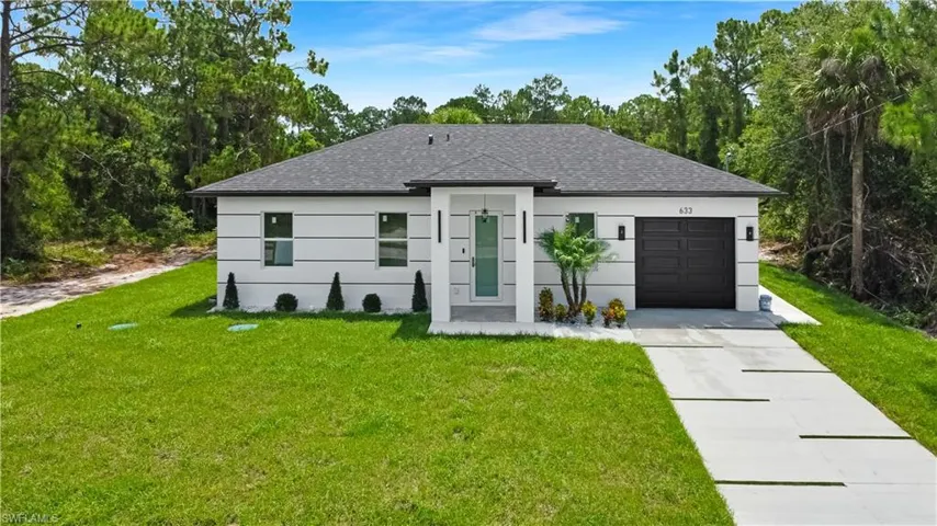 View of front of home with an attached garage, a front yard, concrete driveway, roof with shingles, and view of scattered trees