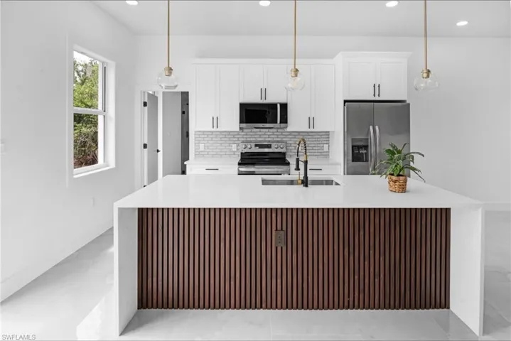Kitchen with light stone counters, stainless steel appliances, a spacious island, and white cabinets