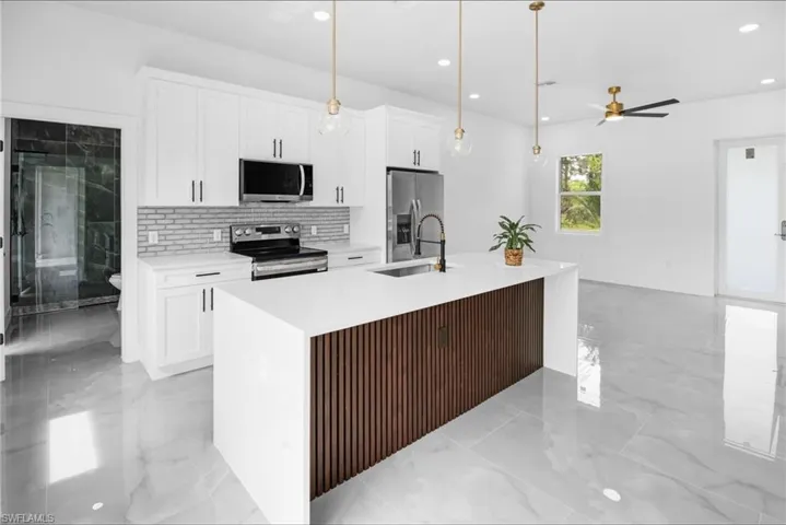 Kitchen featuring a kitchen island with sink, stainless steel appliances, pendant lighting, and light stone counters