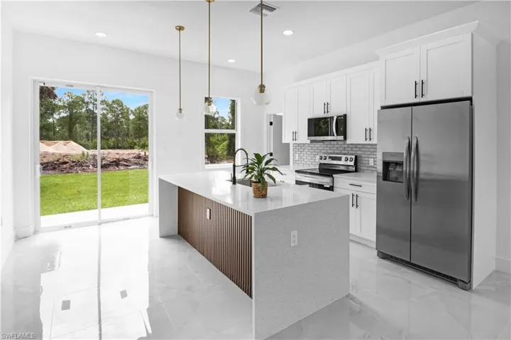 Kitchen featuring stainless steel appliances, light stone countertops, white cabinetry, tasteful backsplash, and an island with sink