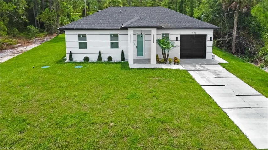 View of front facade featuring a front yard, an attached garage, concrete driveway, and roof with shingles